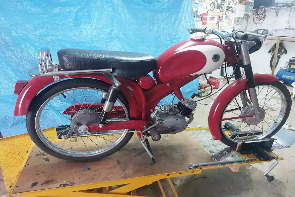 Motocicleta clásica de color rojo y blanco sobre una plataforma de trabajo en un taller con fondo azul Motocicleta clásica de color rojo y blanco sobre una plataforma de trabajo en un taller con fondo azul