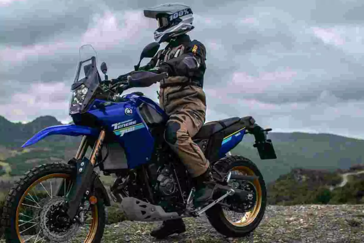 Persona con equipo de motocross conduciendo una motocicleta azul Yamaha Ténéré en un entorno montañoso bajo un cielo nublado Persona con equipo de motocross conduciendo una motocicleta azul Yamaha Ténéré en un entorno montañoso bajo un cielo nublado