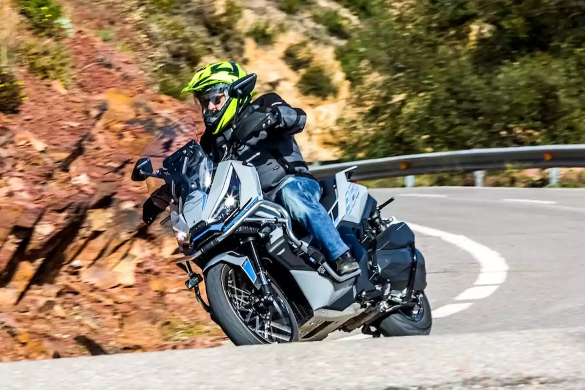 Persona con casco amarillo y chaqueta negra conduciendo un scooter Voge 368G en una carretera de curvas junto a una ladera rocosa Persona con casco amarillo y chaqueta negra conduciendo un scooter Voge 368G en una carretera de curvas junto a una ladera rocosa