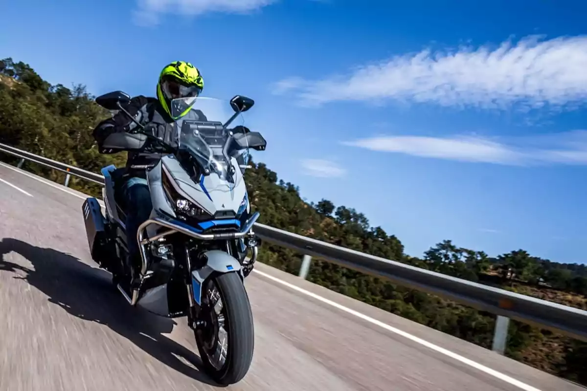 Persona conduciendo una motocicleta en una carretera con cielo azul y árboles al fondo Persona conduciendo una motocicleta en una carretera con cielo azul y árboles al fondo