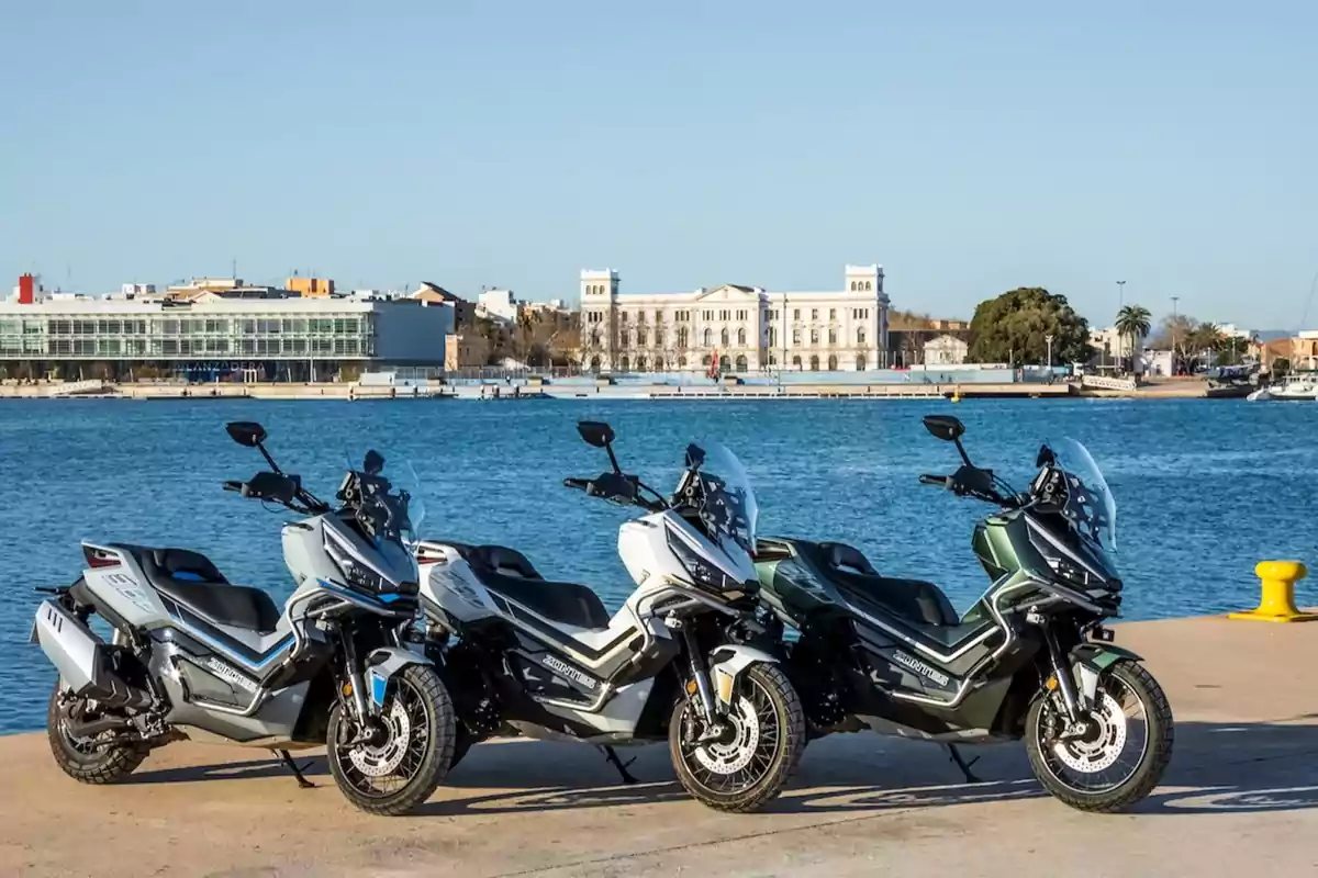 Tres motocicletas tipo scooter estacionadas junto a un muelle con un edificio grande y el mar al fondo Tres motocicletas tipo scooter estacionadas junto a un muelle con un edificio grande y el mar al fondo