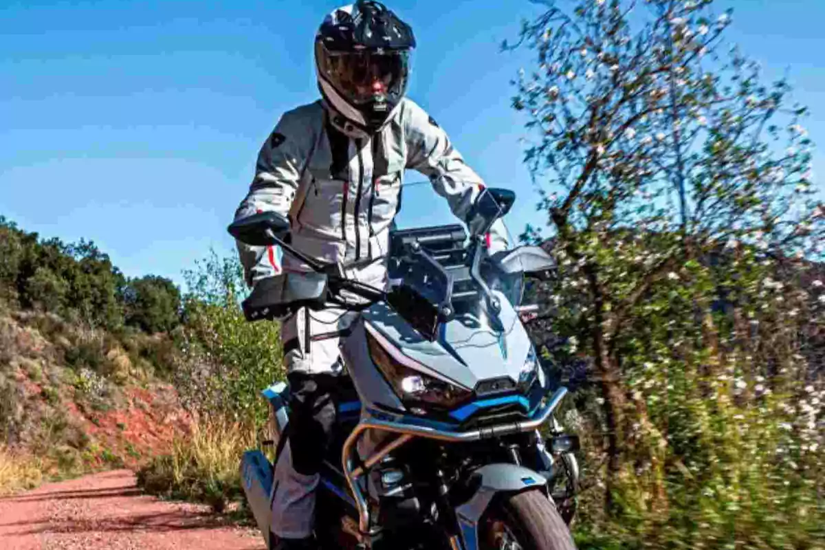 Persona amb vestit i casc de motorista conduint una moto per un camí de terra envoltat de vegetació sota un cel serè Persona amb vestit i casc de motorista conduint una moto per un camí de terra envoltat de vegetació sota un cel serè