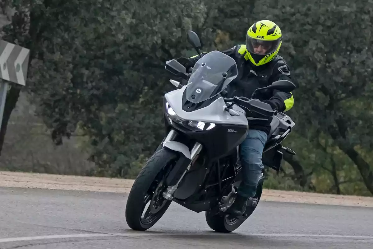 Persona con casco y chaqueta de protección conduciendo una motocicleta en una carretera curva rodeada de árboles Persona con casco y chaqueta de protección conduciendo una motocicleta en una carretera curva rodeada de árboles