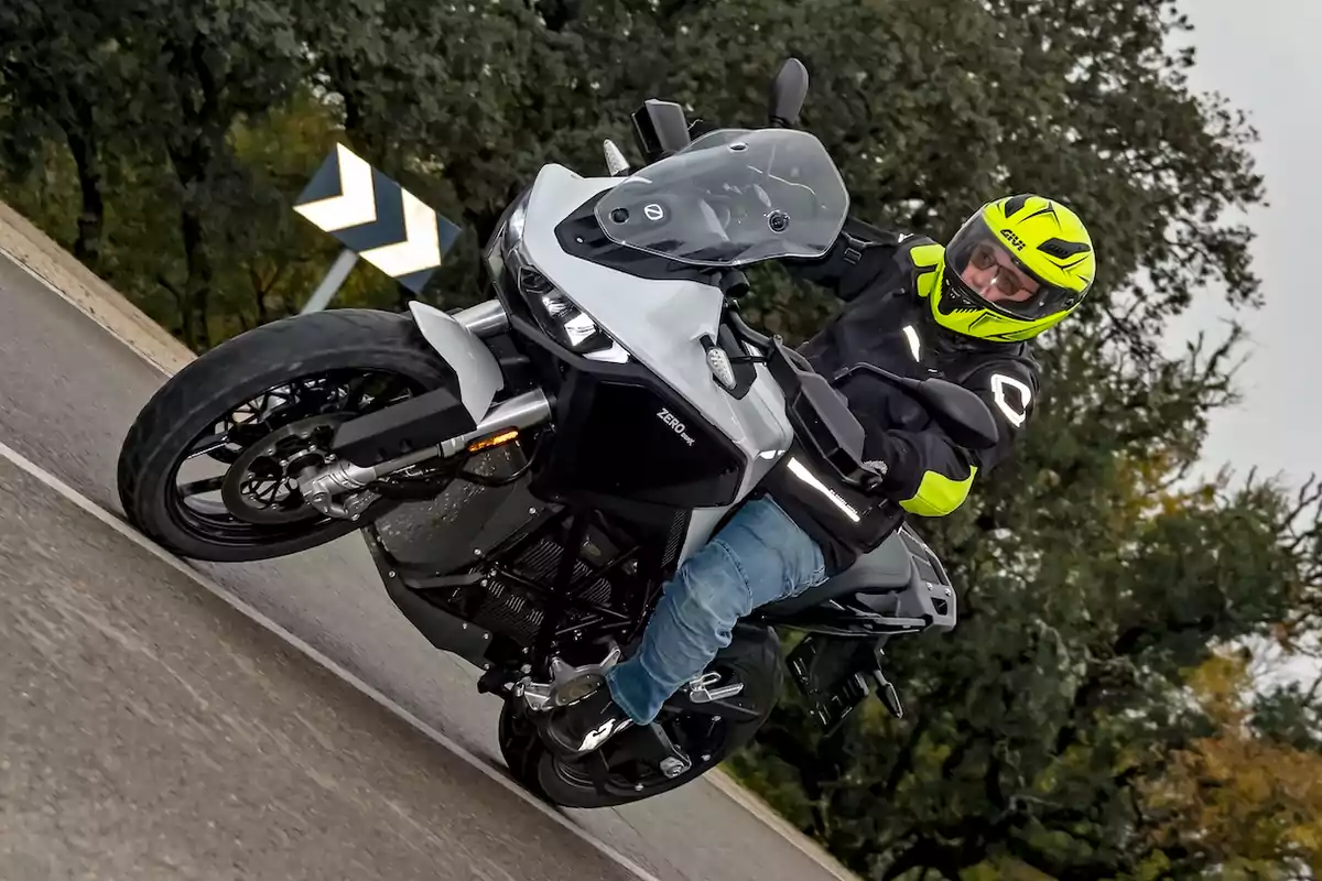 Person wearing a helmet and protective jacket riding a motorcycle on a curve on a road surrounded by trees.