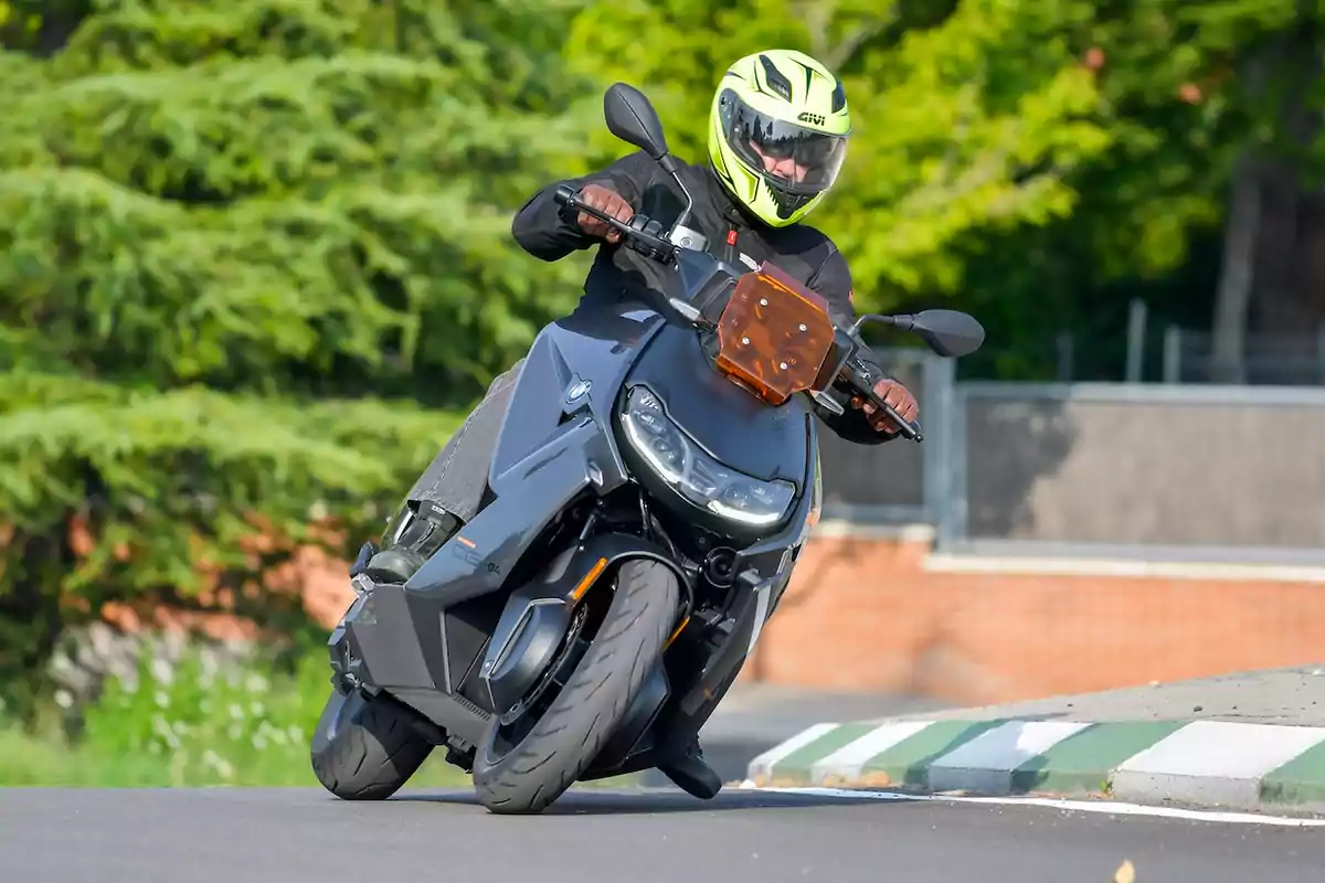 Persona con casco amarillo conduciendo una moto eléctrica negra en una curva sobre asfalto Persona con casco amarillo conduciendo una moto eléctrica negra en una curva sobre asfalto