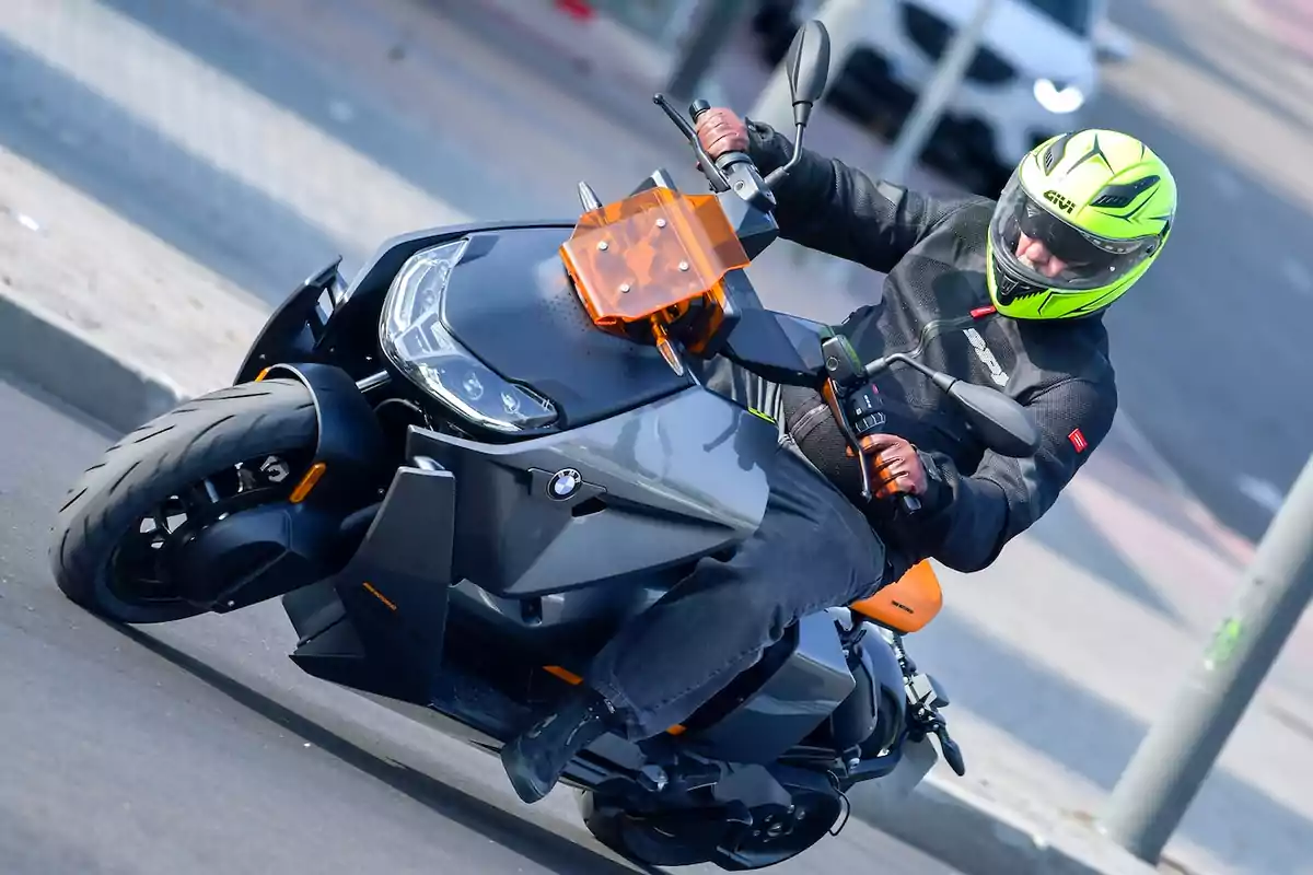 Person wearing a fluorescent yellow helmet and a black jacket riding a gray BMW electric motorcycle on a paved street