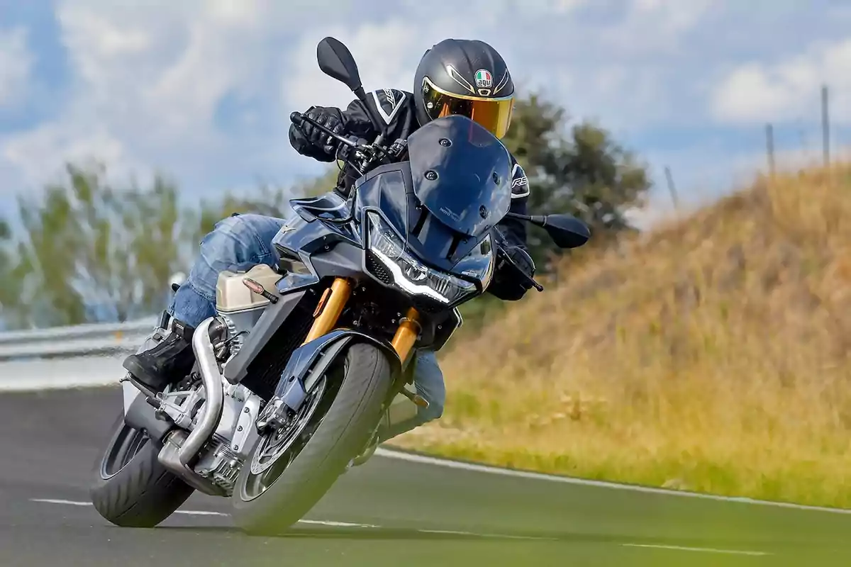 Persona conduciendo una motocicleta deportiva en una carretera curva con fondo de vegetación y cielo parcialmente nublado Persona conduciendo una motocicleta deportiva en una carretera curva con fondo de vegetación y cielo parcialmente nublado