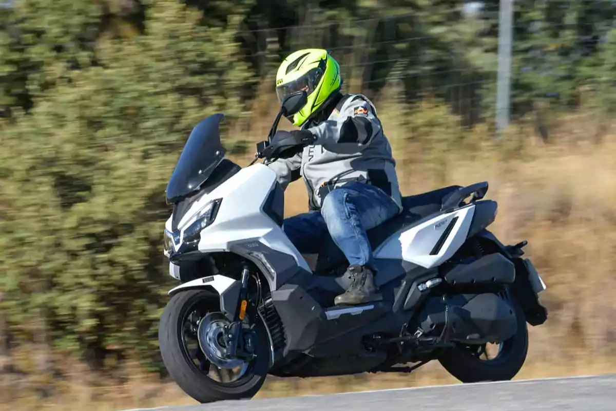 Persona conduciendo una motocicleta tipo scooter blanca en una carretera con vegetación al fondo Persona conduciendo una motocicleta tipo scooter blanca en una carretera con vegetación al fondo