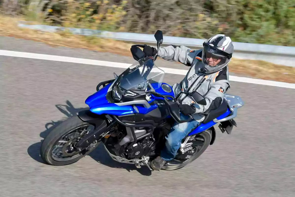 Persona conduint una motocicleta blava per una carretera asfaltada portant casc i jaqueta protectora Persona conduint una motocicleta blava per una carretera asfaltada portant casc i jaqueta protectora