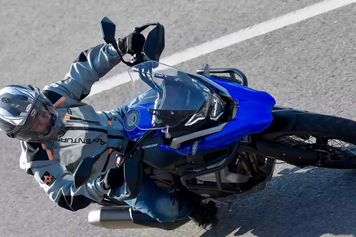 Persona conduint una motocicleta blava per una carretera asfaltada, portant casc i jaqueta de protecció Persona conduint una motocicleta blava per una carretera asfaltada, portant casc i jaqueta de protecció