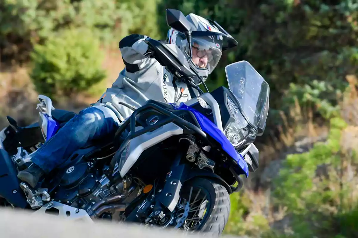 Persona conduciendo una motocicleta azul en una carretera rodeada de vegetación