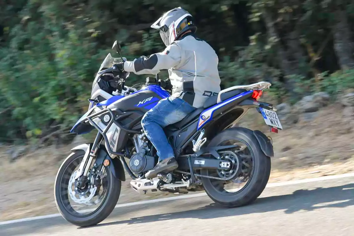 Persona conduint una motocicleta blava per una carretera envoltada de vegetació Persona conduint una motocicleta blava per una carretera envoltada de vegetació