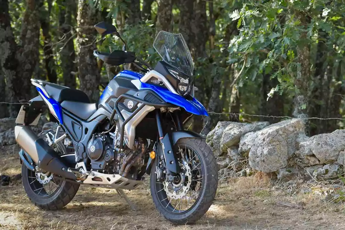 Motocicleta blava tipus trail estacionada en un entorn natural amb arbres i roques al fons Motocicleta blava tipus trail estacionada en un entorn natural amb arbres i roques al fons