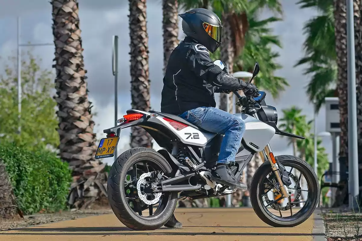 Persona con casco y chaqueta negra conduciendo una motocicleta blanca en una calle con palmeras Persona con casco y chaqueta negra conduciendo una motocicleta blanca en una calle con palmeras