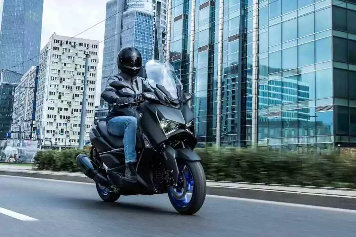 Persona conduciendo una motocicleta negra por una avenida en una ciudad moderna con edificios altos de fondo Persona conduciendo una motocicleta negra por una avenida en una ciudad moderna con edificios altos de fondo