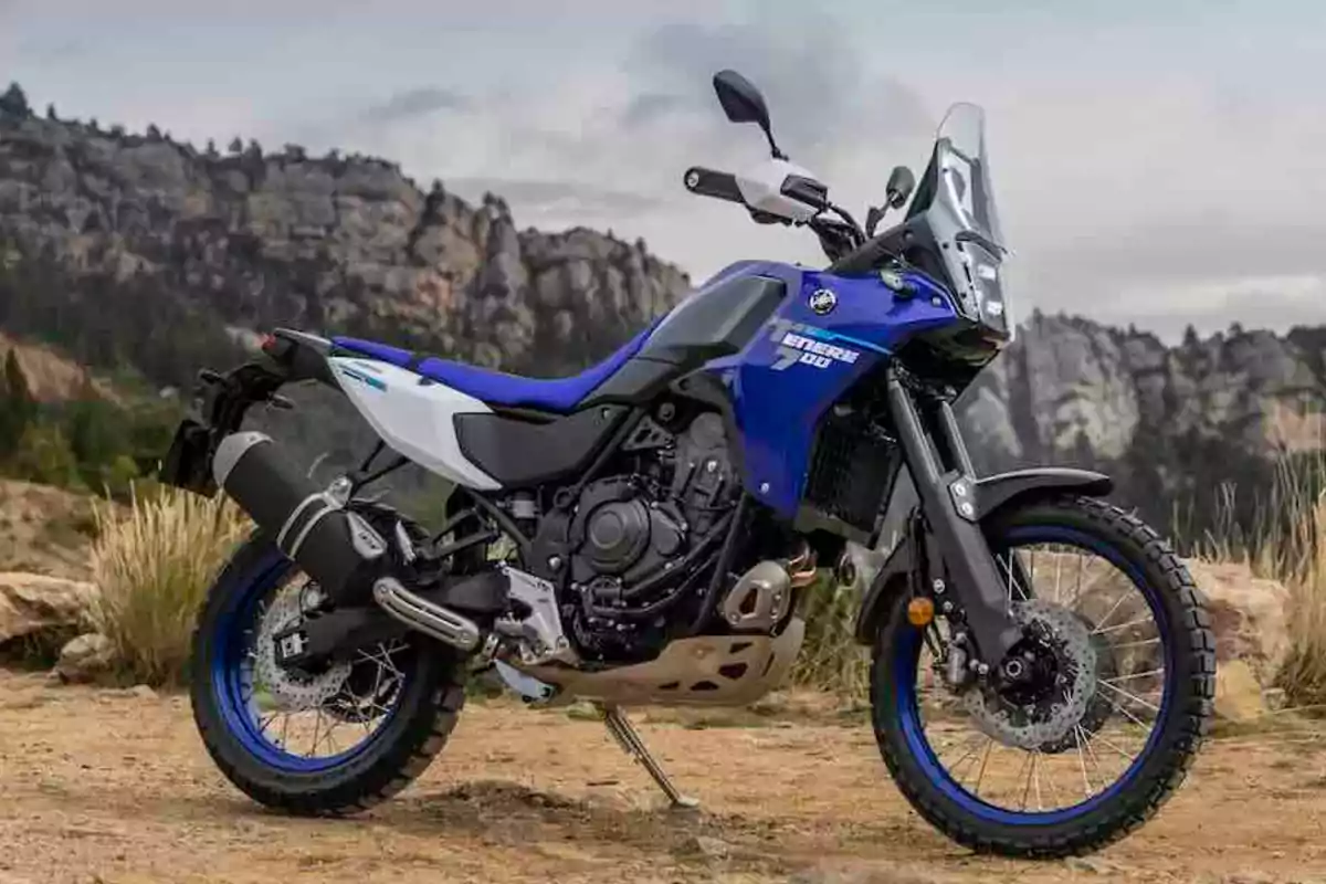 Motocicleta azul y blanca de tipo aventura estacionada en un entorno natural con montañas al fondo Motocicleta azul y blanca de tipo aventura estacionada en un entorno natural con montañas al fondo