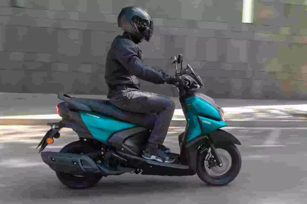Persona conduciendo una motoneta azul con casco y ropa de protección en una calle urbana Persona conduciendo una motoneta azul con casco y ropa de protección en una calle urbana