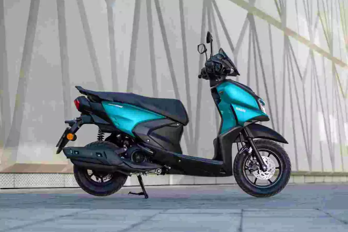 Motocicleta tipo scooter color azul con negro estacionada sobre un pavimento frente a una pared moderna Motocicleta tipo scooter color azul con negro estacionada sobre un pavimento frente a una pared moderna
