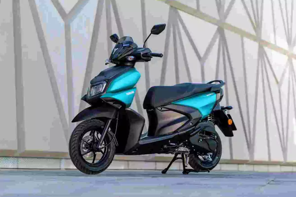 Motocicleta tipo scooter color azul con negro estacionada frente a una pared de diseño geométrico Motocicleta tipo scooter color azul con negro estacionada frente a una pared de diseño geométrico