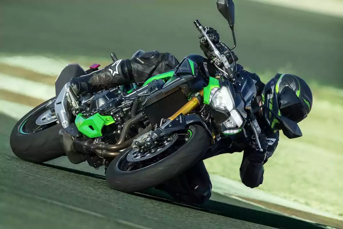 Motociclista inclinado al máximo en una curva mientras conduce una moto deportiva verde y negra en una pista Motociclista inclinado al máximo en una curva mientras conduce una moto deportiva verde y negra en una pista