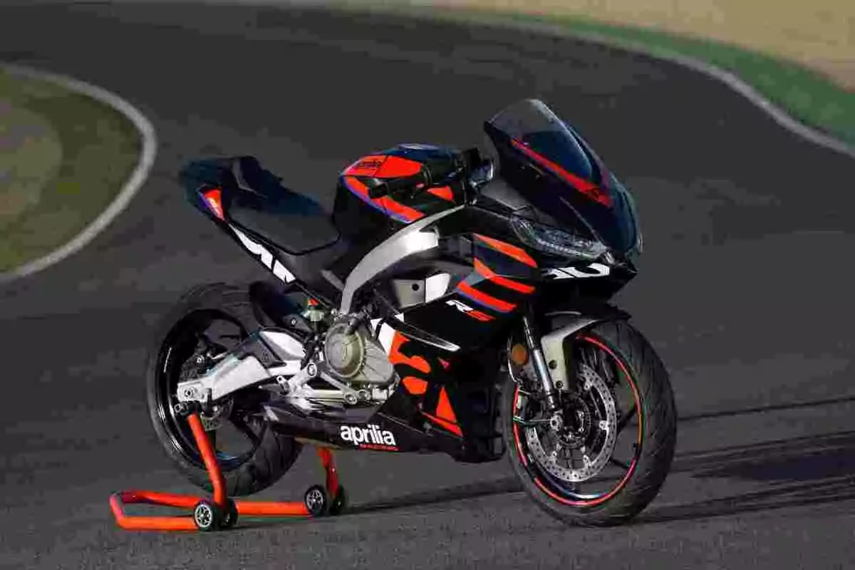 Motocicleta deportiva Aprilia RS 660 en color negro con detalles en rojo y naranja estacionada sobre un soporte en una pista de carreras Motocicleta deportiva Aprilia RS 660 en color negro con detalles en rojo y naranja estacionada sobre un soporte en una pista de carreras