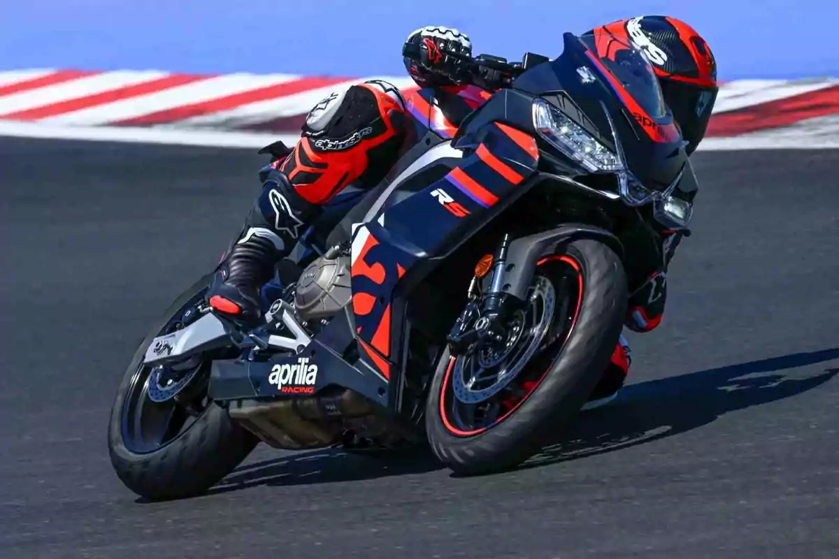 Motociclista con traje y casco rojo y negro conduciendo una moto deportiva Aprilia en una pista de carreras Motociclista con traje y casco rojo y negro conduciendo una moto deportiva Aprilia en una pista de carreras