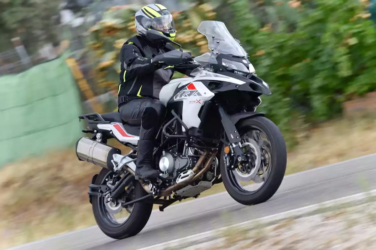 Persona conduint una motocicleta esportiva blanca i negra per una carretera amb vegetació al fons Persona conduint una motocicleta esportiva blanca i negra per una carretera amb vegetació al fons
