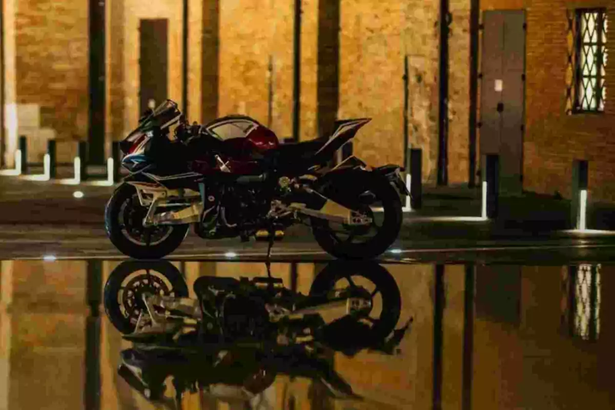 Motocicleta esportiva aparcada davant d’un edifici de maó amb el seu reflex visible en un bassal d’aigua Motocicleta esportiva aparcada davant d’un edifici de maó amb el seu reflex visible en un bassal d’aigua