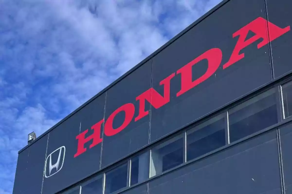 Edificio gris con el logotipo y el nombre de Honda en letras rojas bajo un cielo azul con nubes. Edificio gris con el logotipo y el nombre de Honda en letras rojas bajo un cielo azul con nubes.