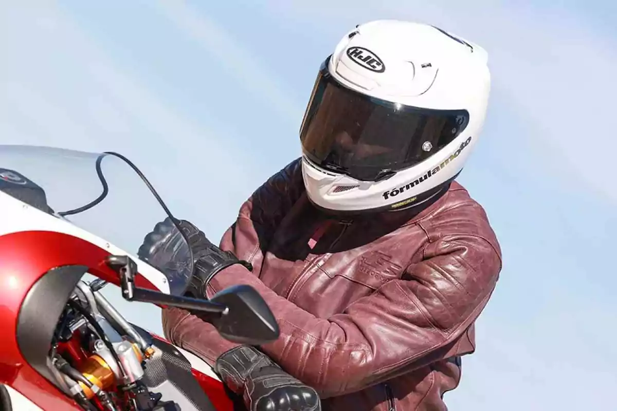 Persona con casco blanco y chaqueta de cuero roja conduciendo una motocicleta roja y blanca Persona con casco blanco y chaqueta de cuero roja conduciendo una motocicleta roja y blanca