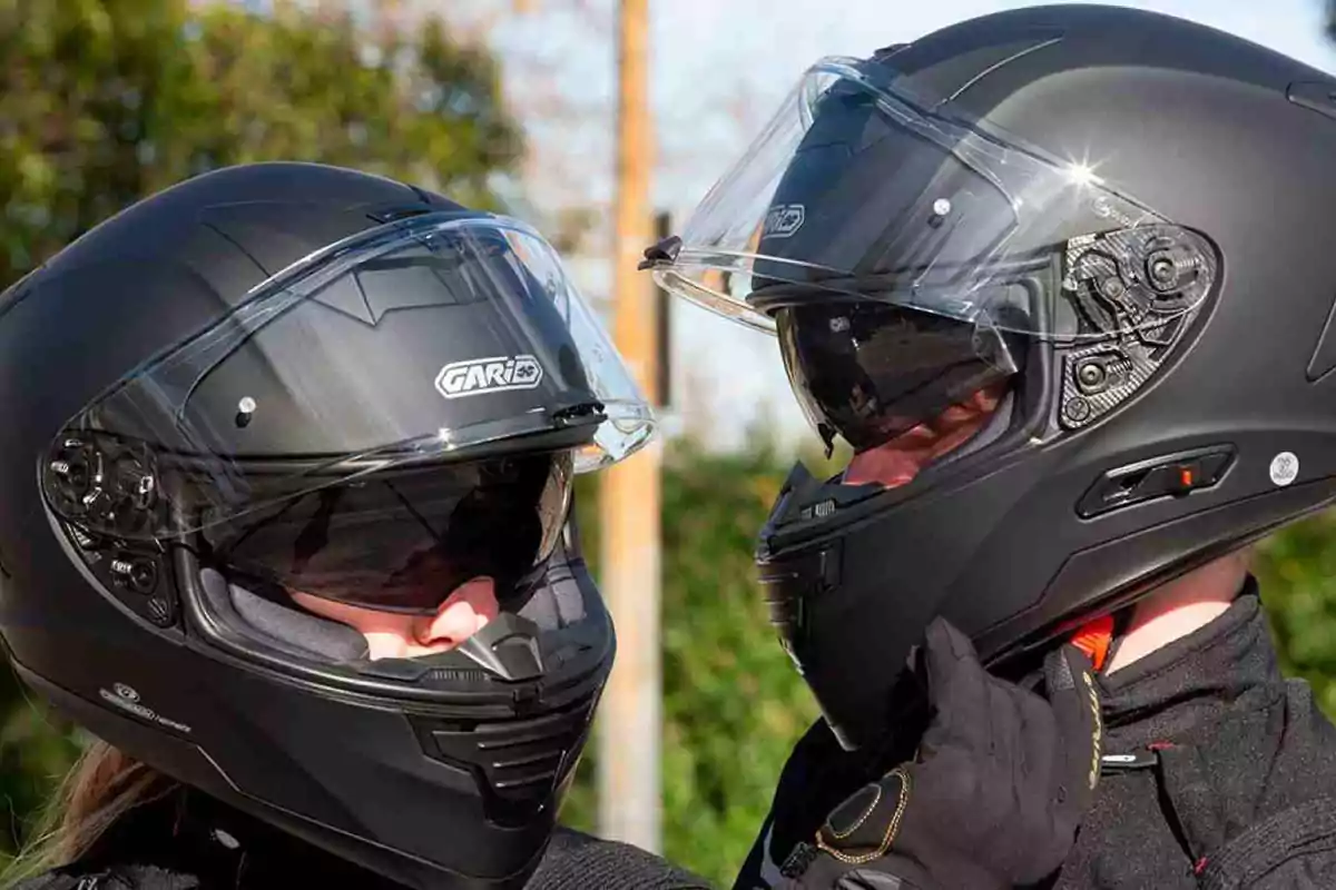 Dos personas usando cascos de motocicleta negros se miran de frente al aire libre Dos personas usando cascos de motocicleta negros se miran de frente al aire libre
