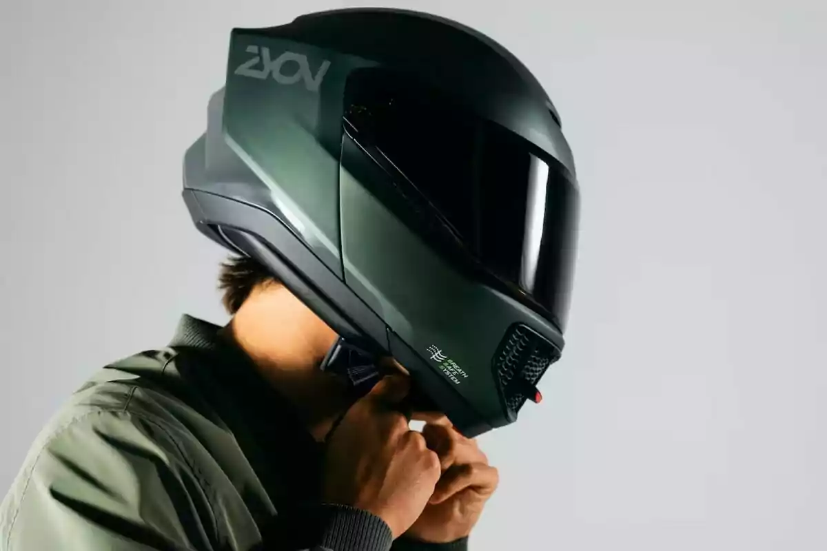 Persona ajustant un casc de motocicleta modern de color verd fosc amb visera negra Persona ajustant un casc de motocicleta modern de color verd fosc amb visera negra
