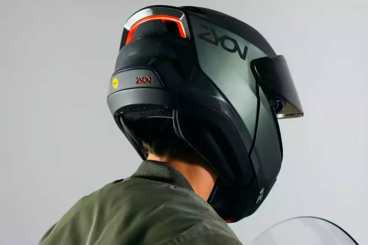 Persona amb un casc de motocicleta negre amb detalls vermells i visera fosca, vista des del darrere Persona amb un casc de motocicleta negre amb detalls vermells i visera fosca, vista des del darrere