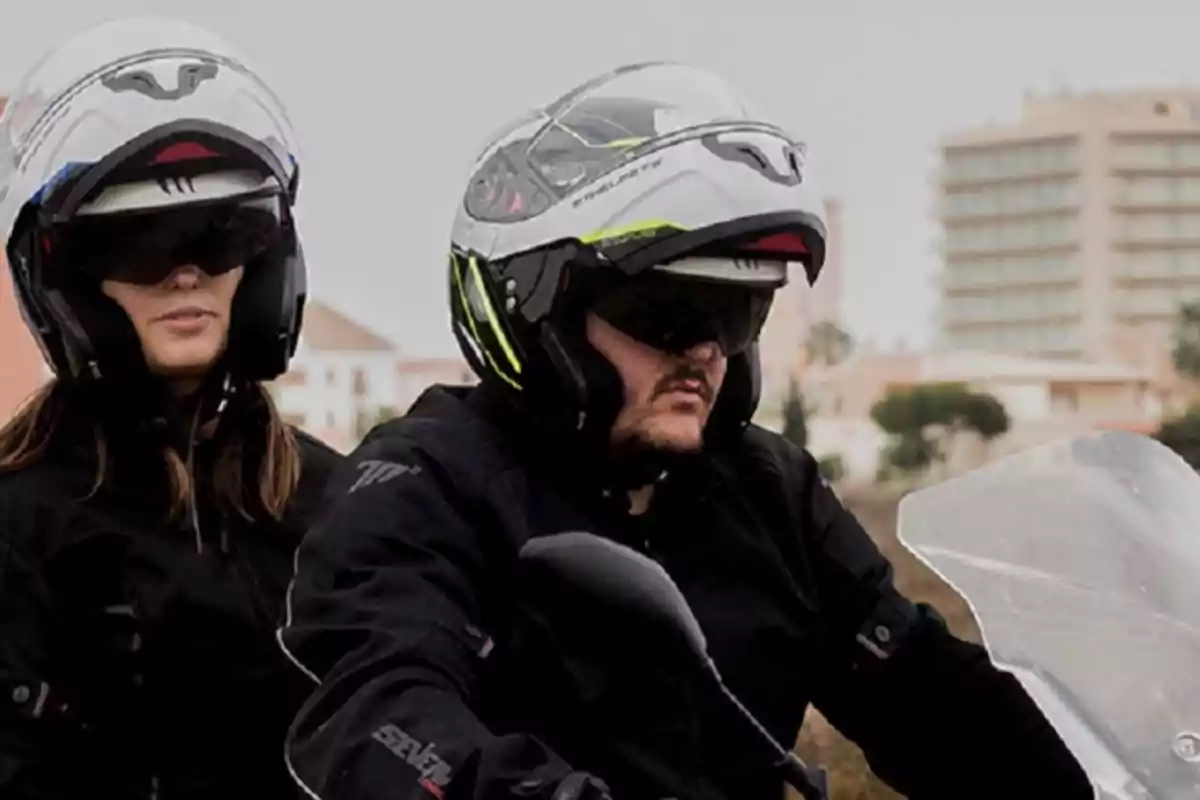 Dues persones amb casc i jaqueta de motorista van en una moto per una ciutat.