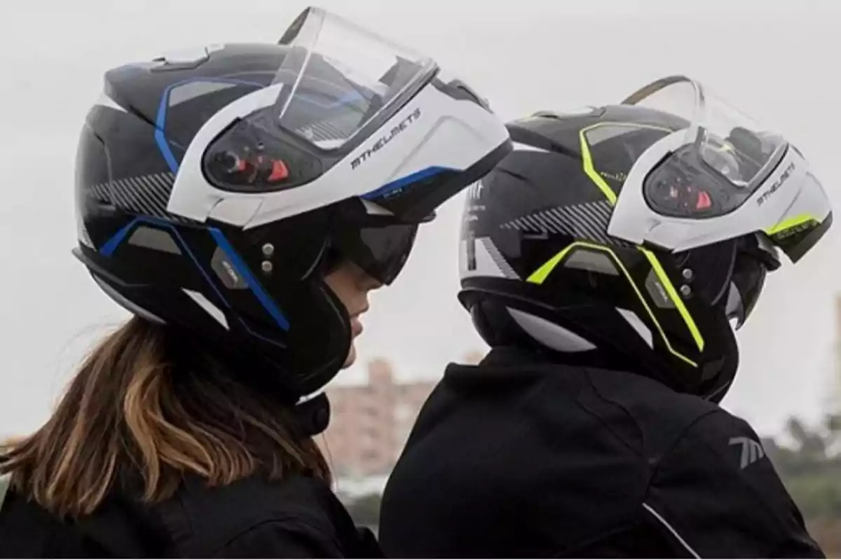 Dues persones amb cascos de moto modulars amb detalls en blau i groc, vistes de perfil i d’esquena Dues persones amb cascos de moto modulars amb detalls en blau i groc, vistes de perfil i d’esquena