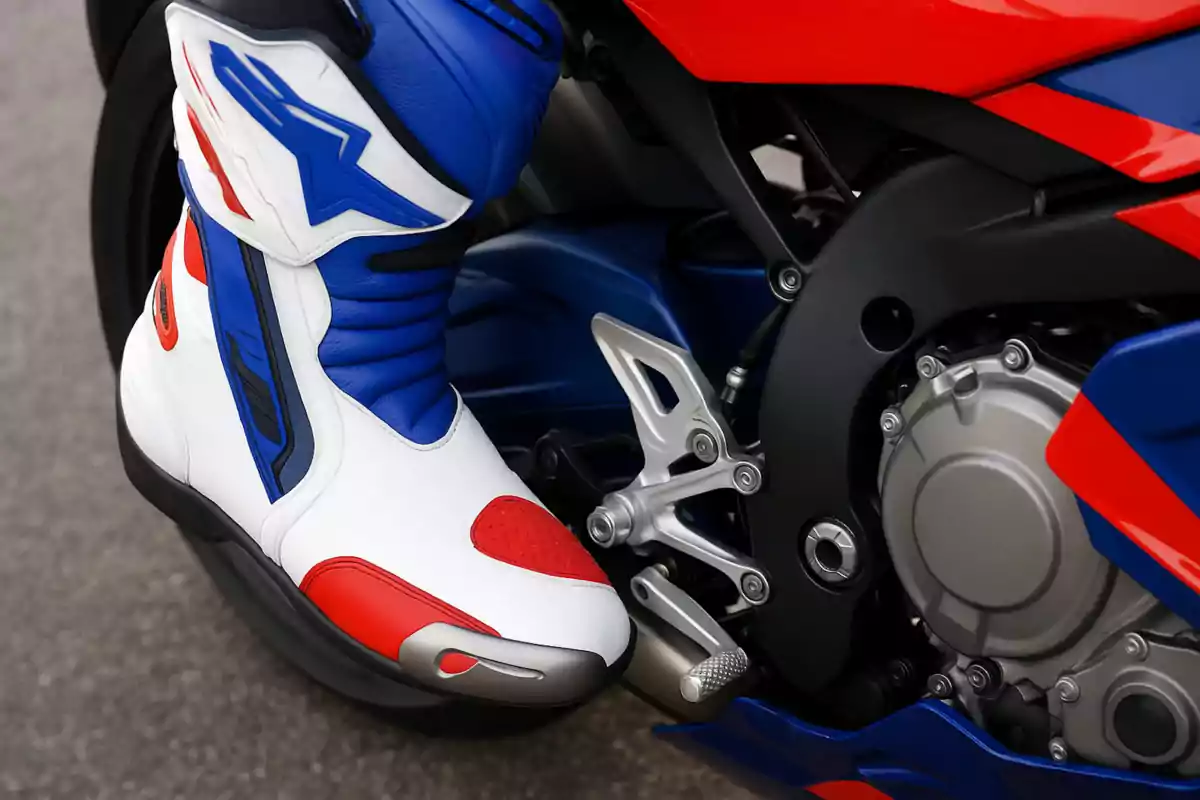 Bota de motociclista deportiva en colores blanco, azul y rojo sobre el pedal de una motocicleta