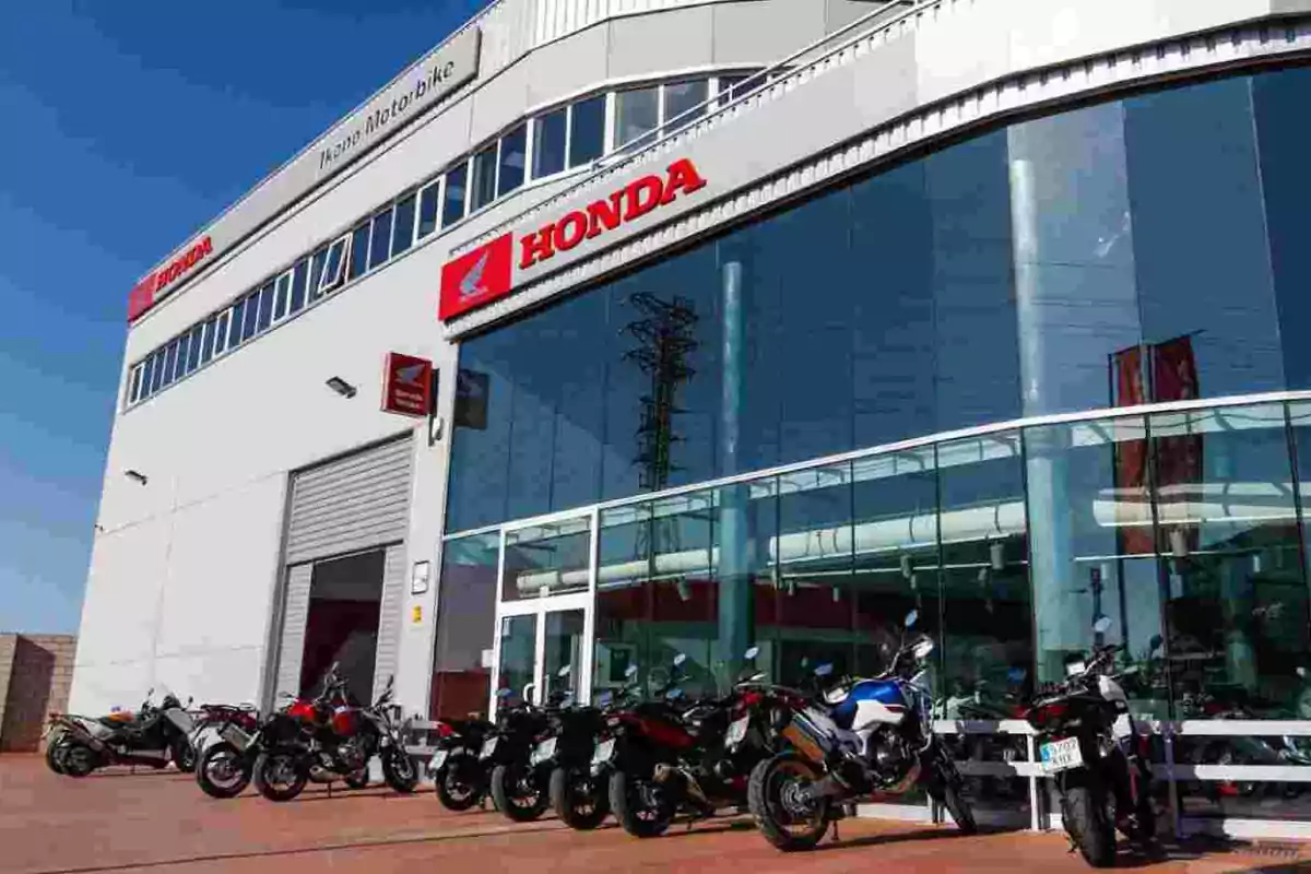 Façana d’una botiga Honda amb diverses motocicletes aparcades al davant i grans finestrals que reflecteixen el cel blau Façana d’una botiga Honda amb diverses motocicletes aparcades al davant i grans finestrals que reflecteixen el cel blau