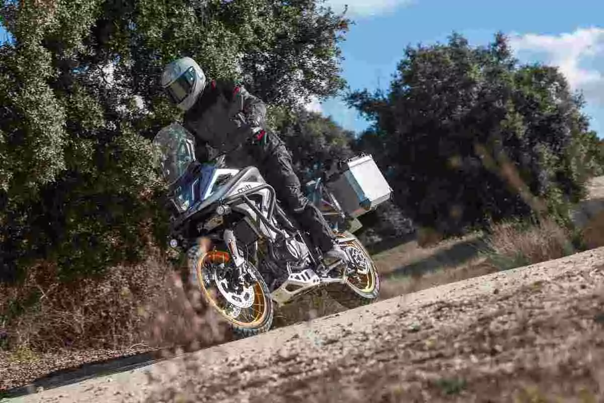 Person riding an adventure motorcycle on a dirt road surrounded by trees Person riding an adventure motorcycle on a dirt road surrounded by trees