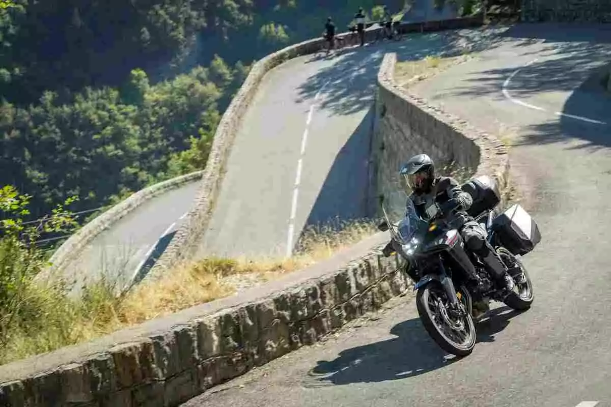 Person riding a motorcycle on a mountain road with sharp curves and cyclists in the background Person riding a motorcycle on a mountain road with sharp curves and cyclists in the background