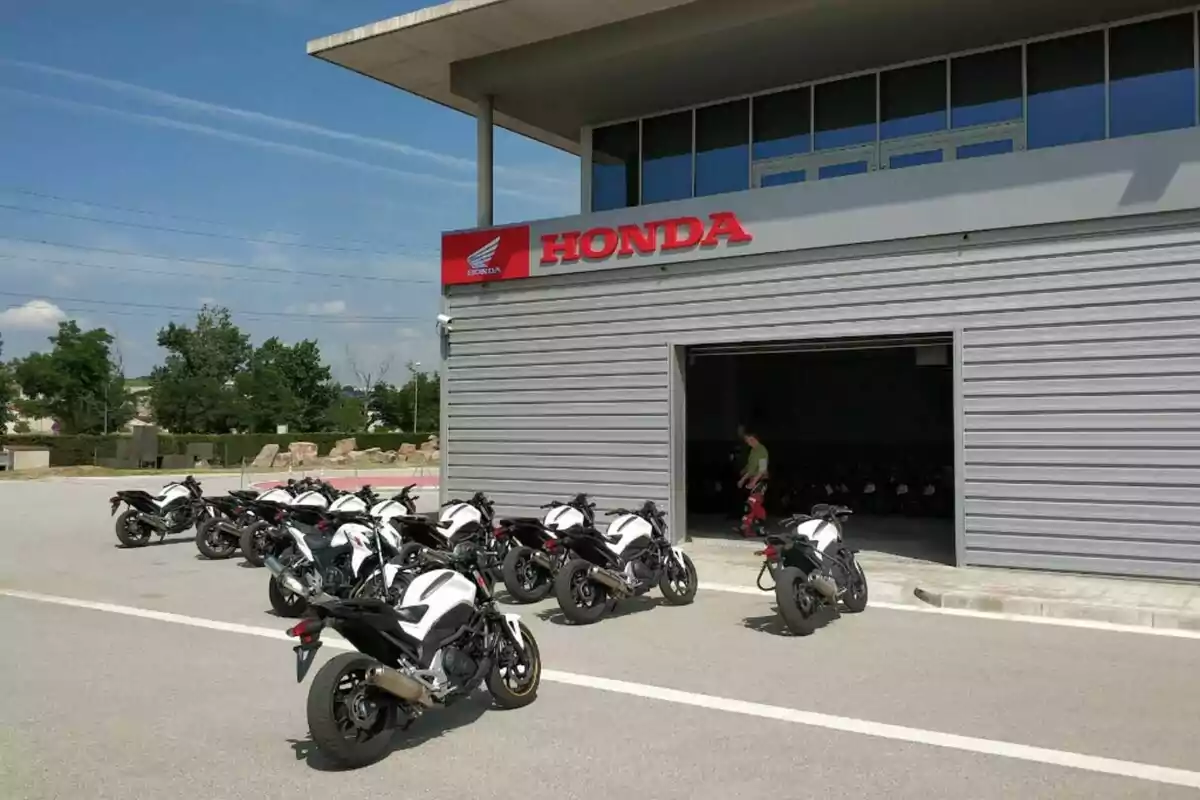 Varios motocicletas Honda blancas estacionadas frente a una concesionaria Honda con una persona cerca de la entrada. Varios motocicletas Honda blancas estacionadas frente a una concesionaria Honda con una persona cerca de la entrada.