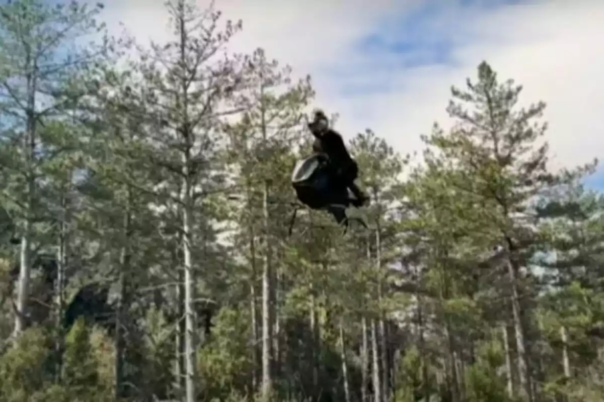 Persona volando sobre un dron grande en medio de un bosque con árboles altos y cielo parcialmente nublado. Persona volando sobre un dron grande en medio de un bosque con árboles altos y cielo parcialmente nublado.