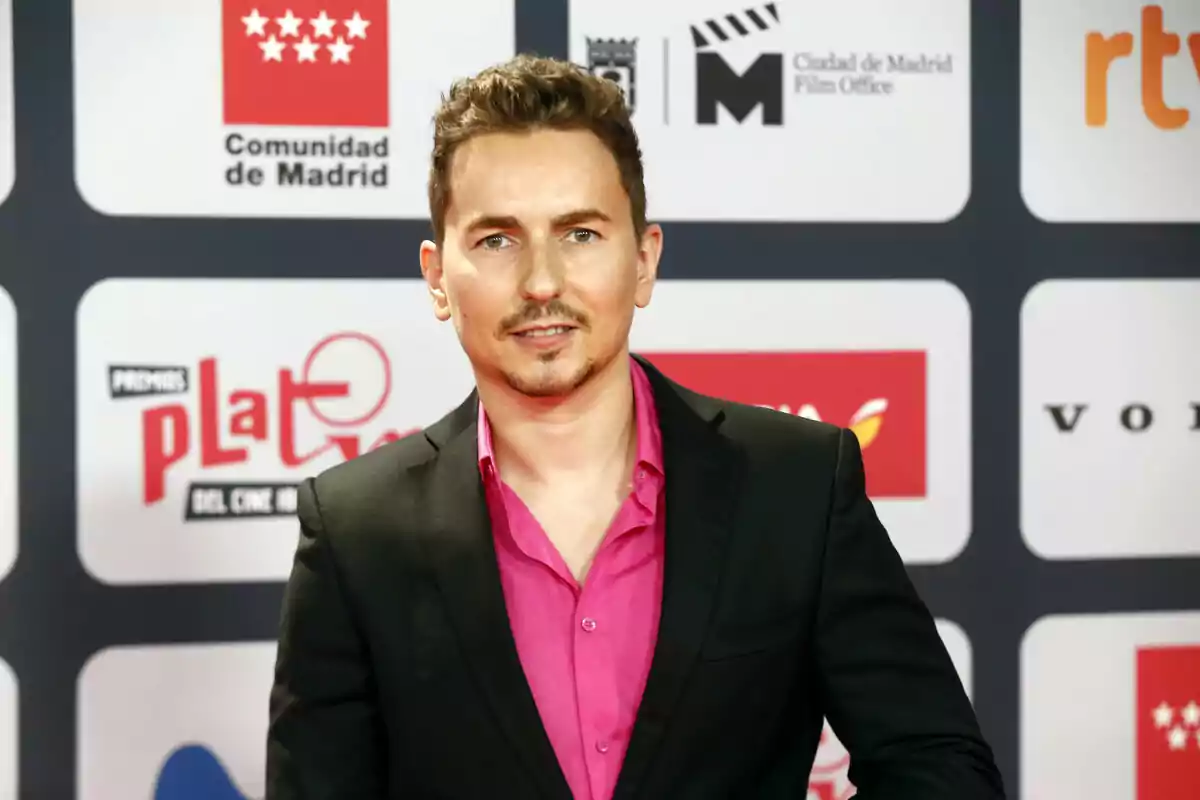 Jorge Lorenzo con saco negro y camisa rosa posando en una alfombra roja frente a un fondo con logotipos de patrocinadores. Jorge Lorenzo con saco negro y camisa rosa posando en una alfombra roja frente a un fondo con logotipos de patrocinadores.