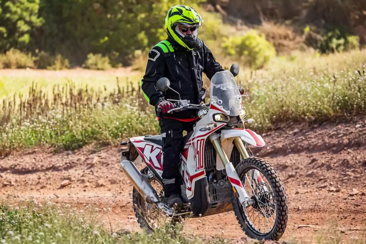 Persona amb casc i equip de protecció conduint una motocicleta d'enduro per un camí de terra envoltat de vegetació Persona amb casc i equip de protecció conduint una motocicleta d'enduro per un camí de terra envoltat de vegetació