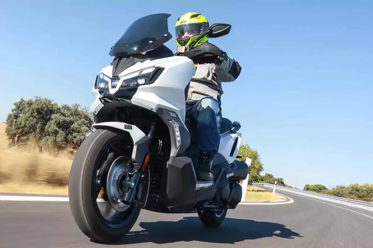 Persona conduciendo una motocicleta blanca en una carretera curva bajo un cielo despejado