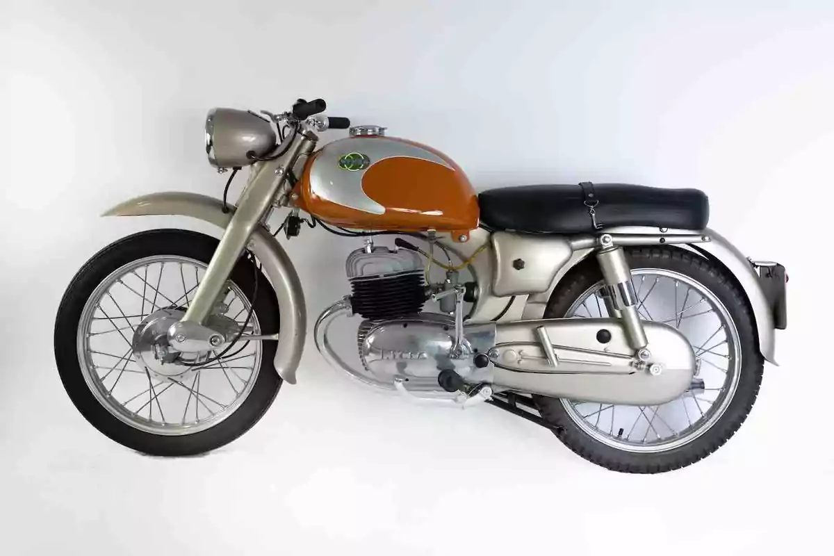 Motocicleta clásica de color naranja y plateado con asiento negro sobre un fondo blanco Motocicleta clásica de color naranja y plateado con asiento negro sobre un fondo blanco