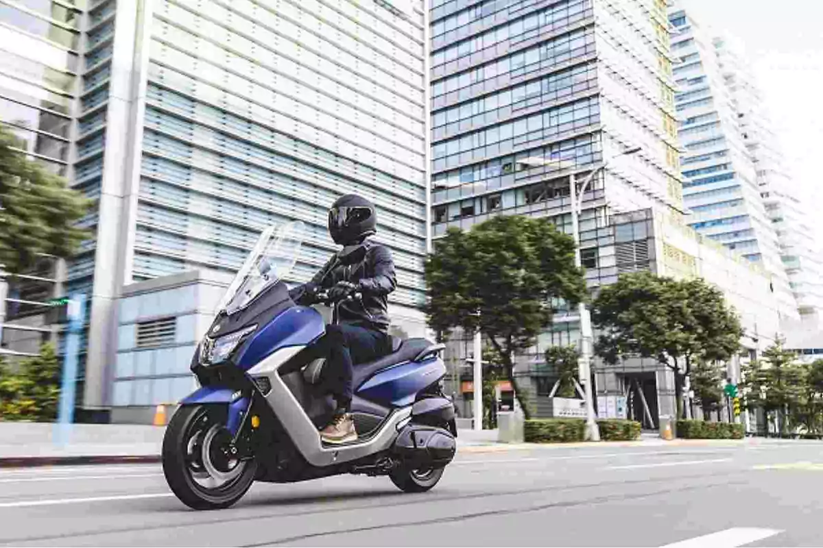 Persona conduciendo una motocicleta azul por una avenida en una ciudad moderna con edificios altos y árboles a los lados Persona conduciendo una motocicleta azul por una avenida en una ciudad moderna con edificios altos y árboles a los lados