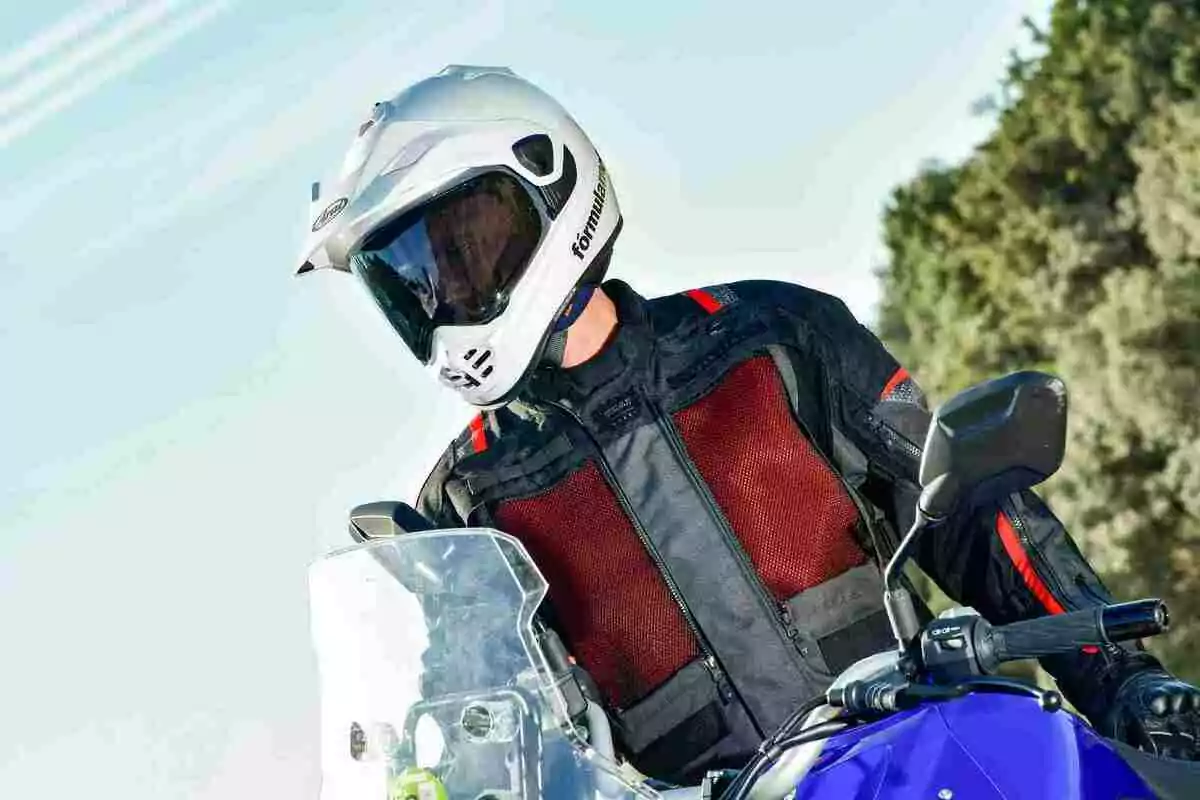 Persona amb casc blanc i jaqueta de protecció negra i vermella conduint una motocicleta blava en un entorn a l’aire lliure Persona amb casc blanc i jaqueta de protecció negra i vermella conduint una motocicleta blava en un entorn a l’aire lliure