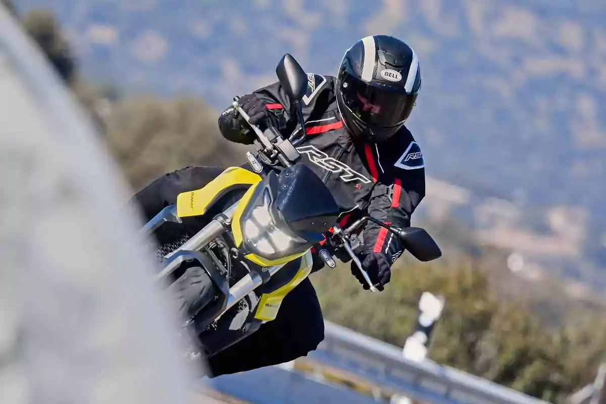 Persona amb casc i jaqueta de motorista conduint una moto groga per una carretera amb corba Persona amb casc i jaqueta de motorista conduint una moto groga per una carretera amb corba