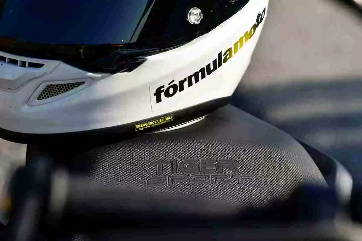 Casc blanc amb la paraula formulamoto recolzat sobre el seient d’una motocicleta Tiger Sport Casc blanc amb la paraula formulamoto recolzat sobre el seient d’una motocicleta Tiger Sport