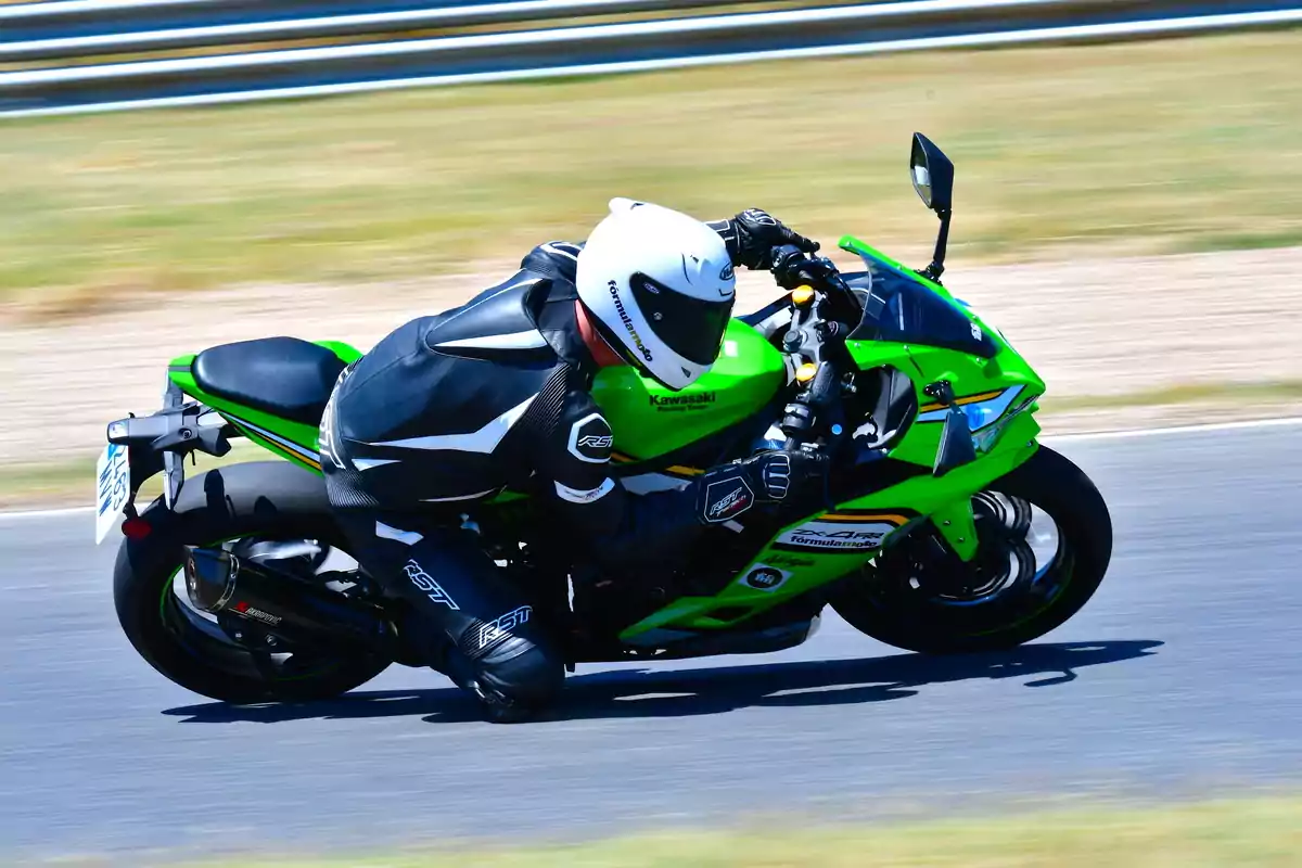 Persona con traje y casco de protección conduciendo una motocicleta deportiva verde en una pista de carreras Persona con traje y casco de protección conduciendo una motocicleta deportiva verde en una pista de carreras